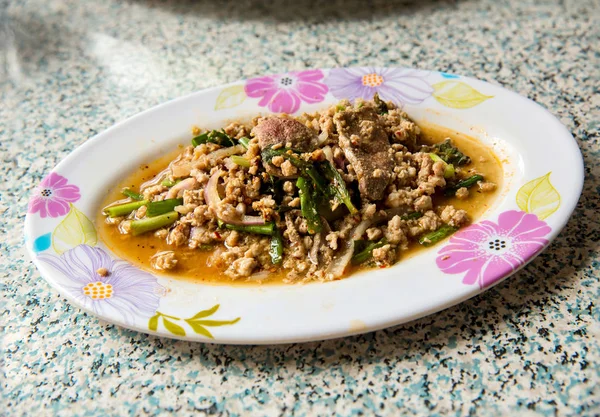 Thai tradition food. Spicy minced pork salad  in white plate on wooden table. Popular with sticky rice and papaya salad. Thai style food. mashed pork, chilli, onion, lemon and cooked herbs.