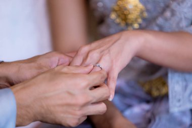 Evlilik yüzükleri. Alyansı ona taktı. Damat, yüzüğü geline tak. Tayland düğün töreni ve Tayland düğün süsü. Damat, yüzüğü gelinin parmağına tak..