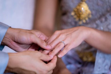Evlilik yüzükleri. Alyansı ona taktı. Damat, yüzüğü geline tak. Tayland düğün töreni ve Tayland düğün süsü. Damat, yüzüğü gelinin parmağına tak..