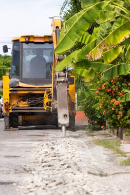 Kazıcı tamir için beton yolu kırıyor ve deliyor. İnşaat malzemelerinin hidrolik koluna monte edilmiş büyük bir pnömatik çekiç. Yol onarım araçları. Delinen matkap.