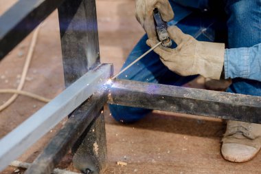 Kaynak makinesi ile metal kaynak yapan bir adam. Kaynakçı mesleği. İnşaat alanında çelik yay döşeme. İş yerinde demir kaynakçılığı yapan endüstri işçisi.