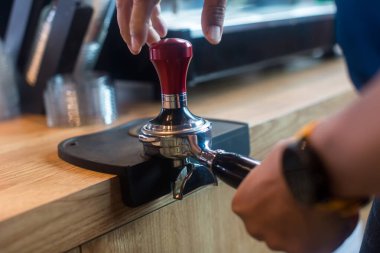 Barista kahve tutacağına kahve bastırıyor. Kahve karıştırıcının üzerine kahve tozu. Barista espresso yapmak için portatif filtreye kahve bastırmak için kurcalayıcı kullanıyor..