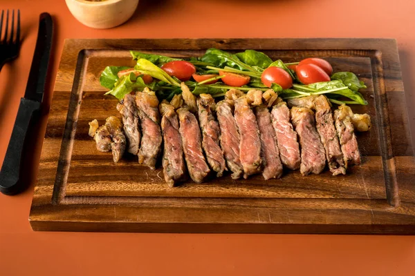 Beef steak on a wooden background. Sliced grilled meat barbecue steak Strip loin with knife and fork carving set on wooden Cutting board.Sliced freshly cooked steak with blood.