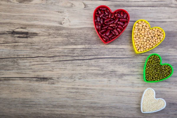 Red beans in red heart shaped plastic bowl. White sesame seeds in white heart shaped. Soybean in yellow heart shaped. Green beans in green heart shaped. Good Food and Health Concept.