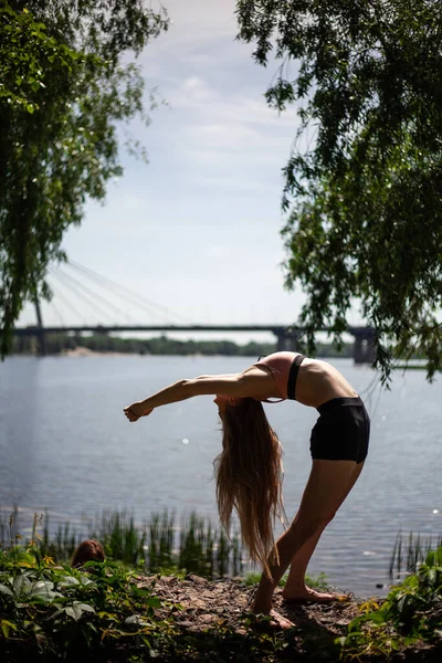 Sportif genç bayan esneme hareketleri yapıyor. İnce kız doğa üzerinde yoga yapıyor, mavi gökyüzü. Sakin, sakin, sağlıklı yaşam tarzı konsepti