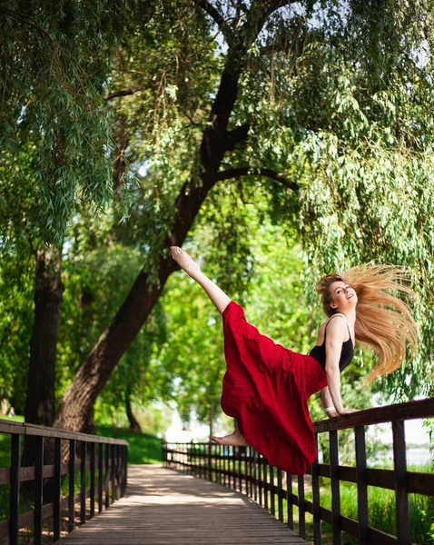 一个年轻的肚皮舞者在公园里的照片 年轻的金发姑娘跳了一跳 穿着红色裙子的女体操运动员 — 图库照片