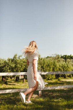 Doğada yürüyen beyaz elbiseli bir kız. Çiftlikte hareket eden bir sarışın. Genç bir kız yazın tadını çıkarıyor..