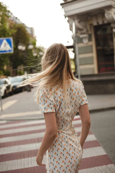 Şehir manzarasının arka planında arkadan çekilmiş bir kızın portresi. Sarışın bir kız şehirde yaz günü yürüyor.