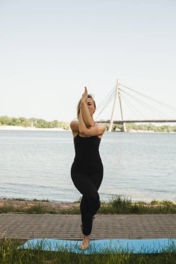 Parkta yoga yapan muhteşem bir genç kadının portresi. Siyah dar takım elbiseli güzel bir kız. Sakin ol ve rahatla, kadınsı mutluluk. Yatay, bulanık arkaplan.