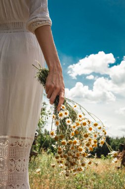 Beyaz elbiseli bir kadın elinde bir buket papatya tutuyor..