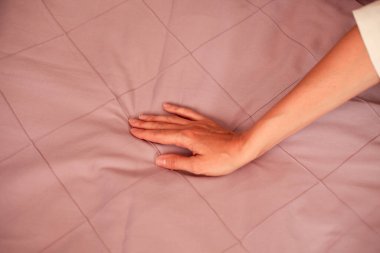 Pembe bir yatağın arka planında bir kadın eli. Yakın plan fotoğraf.