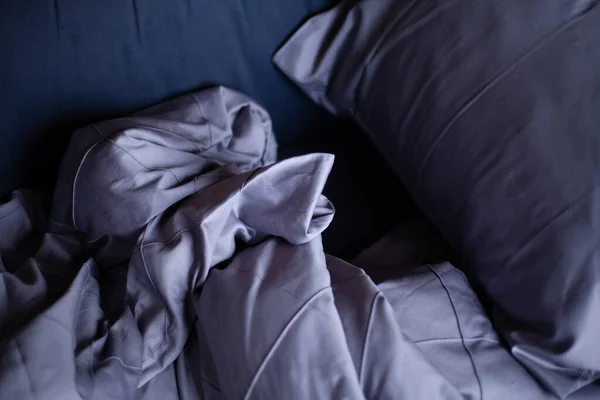 Yapılmamış boş yatak. Yatak örtüsü koyu mavi..