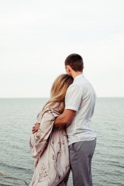 Hamile bir kadın ve kocası denizin arka planına sarılıyorlar. Yazı için yer