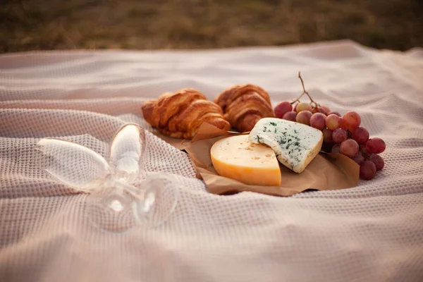 日落时两个人的浪漫野餐 毯子上有两块奶酪 两个羊角面包和两个空杯子 特写照片 图库图片