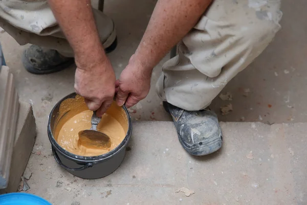 A worker mixes hand-dry cement grout in meringue color with water using a trowel. To fill the gaps between the ceramic tiles.