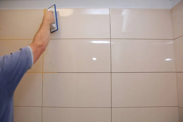 After laying the tiles on the wall, you must fill the spaces between the tiles, a special cement mass or fugue.Renovation works in the bathroom. Grouting of laid tiles using hand tools. A special cement mass to fill gaps between the laid ceramics.