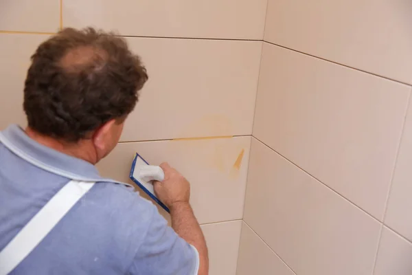 After laying the tiles on the wall, you must fill the spaces between the tiles, a special cement mass or fugue.Renovation works in the bathroom. Grouting of laid tiles using hand tools. A special cement mass to fill gaps between the laid ceramics.