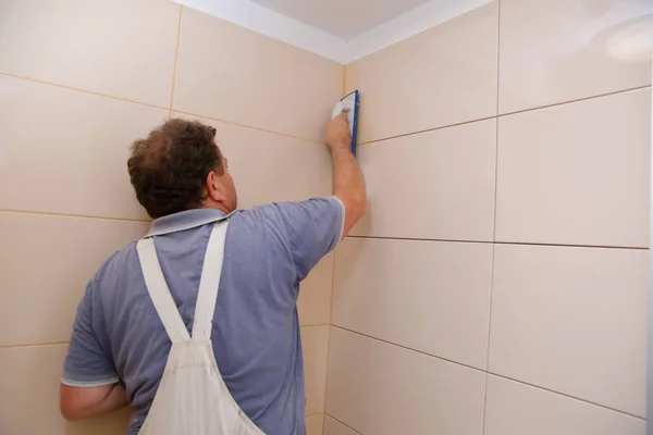 After laying the tiles on the wall, you must fill the spaces between the tiles, a special cement mass or fugue.Renovation works in the bathroom. Grouting of laid tiles using hand tools. A special cement mass to fill gaps between the laid ceramics.