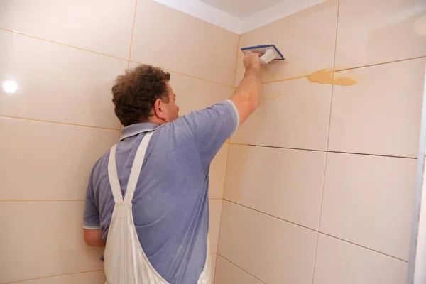 After laying the tiles on the wall, you must fill the spaces between the tiles, a special cement mass or fugue.Renovation works in the bathroom. Grouting of laid tiles using hand tools. A special cement mass to fill gaps between the laid ceramics.