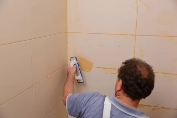 After laying the tiles on the wall, you must fill the spaces between the tiles, a special cement mass or fugue.Renovation works in the bathroom. Grouting of laid tiles using hand tools. A special cement mass to fill gaps between the laid ceramics.