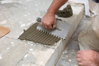 İnşaat işçisi, özel bir el aleti kullanarak merdiven yüzeyini çimento yapıştırıcı kütle ile eşit olarak ayırır..