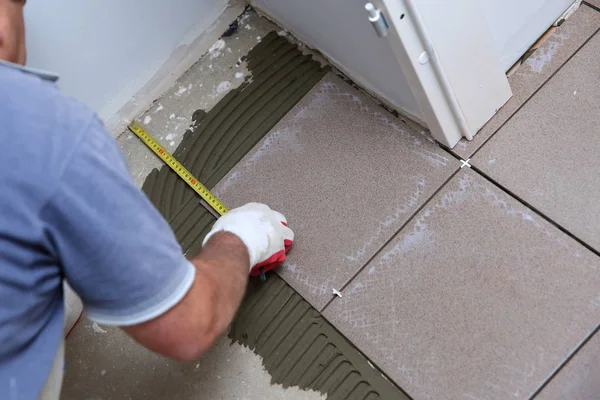 The builder measures the floor with a scoop to arrange the laying of ceramic tiles on the stairs well.