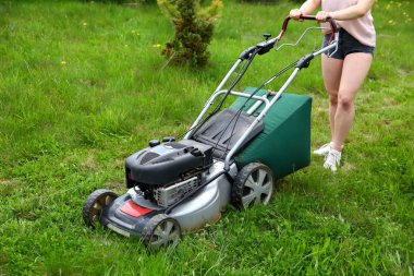 Genç kız bir Benzinli çim biçme makinesi yardımıyla yeşil yüksek ot budama.