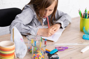 Dersteki kıza bir oyuncak ayı çizme görevi verildi. Genç liseli kız okul defterine pastel boyalarla resim çiziyor..