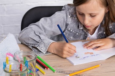 Dersteki kıza bir oyuncak ayı çizme görevi verildi. Genç liseli kız okul defterine pastel boyalarla resim çiziyor..