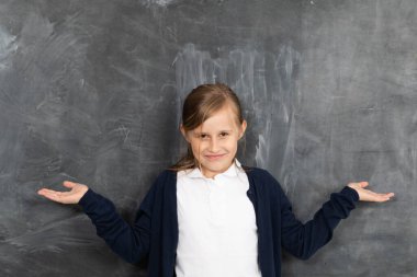A girl stands smiling at a chalkboard and points to an empty space ready for writing with chalk. clipart