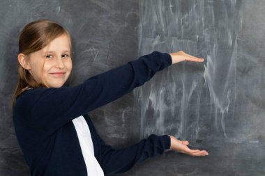 Bir kız tahtaya gülümsüyor ve tebeşirle yazılmaya hazır boş bir yeri işaret ediyor..