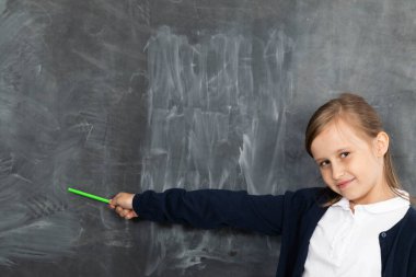Bir kız tahtaya gülümsüyor ve tebeşirle yazılmaya hazır boş bir yeri işaret ediyor..