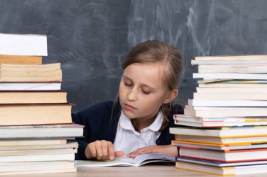 Kız, en iyi olmak istedikleri için önemli sınavları öğrenmek için kitap yığınının arasında oturuyor..