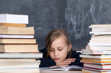 Kız, en iyi olmak istedikleri için önemli sınavları öğrenmek için kitap yığınının arasında oturuyor..