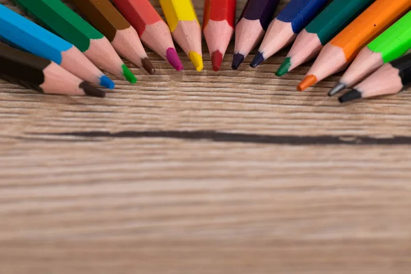 Colored pencil crayons arranged evenly on a wooden desk top. School supplies.