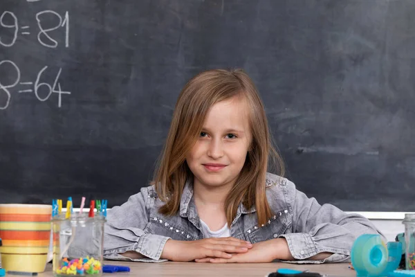 Exemplary schoolgirl. Correct posture while sitting in the classroom. Primary school. Black school board.