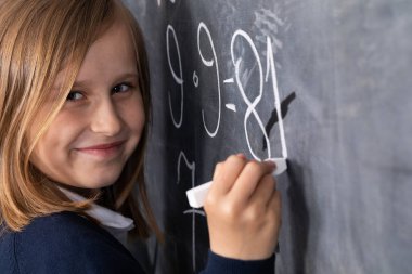 Tahtaya tebeşirle yazı yazıyor. Matematik problemi. Tahtadaki kız..