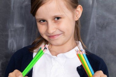 İlkokul. Kız bankta oturuyor ve elinde pastel boyalarla.