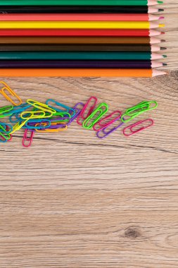 Renkli ataç ve kalemler ahşap bir masanın üstünde yatıyor. Yeni okul aksesuarları.