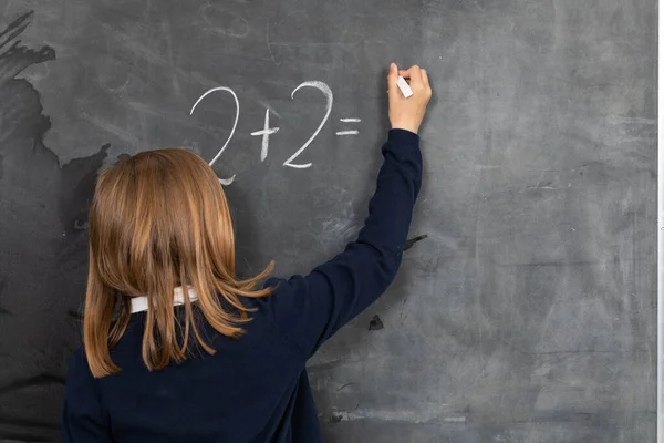 He writes on the chalkboard with chalk. Math problem. A girl at the chalkboard.