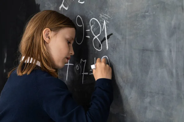 He writes on the chalkboard with chalk. Math problem. A girl at the chalkboard.