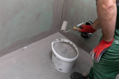 Bir inşaat işçisi boya silindirini sıvı nem izolasyonuyla dolu bir kovada ıslatıyor. İş sırasında..