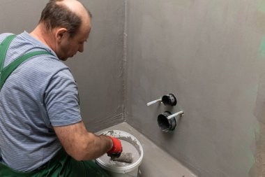 Bir inşaat işçisi boya silindirini sıvı nem izolasyonuyla dolu bir kovada ıslatıyor. İş sırasında..