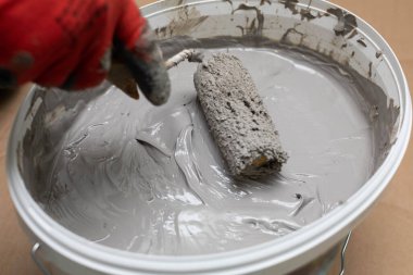 Profesyonel bir inşaat işçisi boya silindirini sıvı nem izolasyonuyla dolu bir kovada ıslatır. İş sırasında. Yakın çekim görünümü.