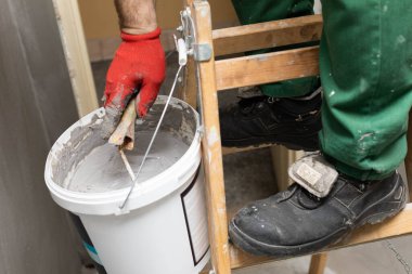 Profesyonel bir inşaat işçisi boya silindirini sıvı nem izolasyonuyla dolu bir kovada ıslatır. İş sırasında. Yakın çekim görünümü.