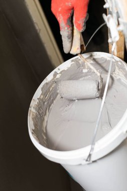 Profesyonel bir inşaat işçisi boya silindirini sıvı nem izolasyonuyla dolu bir kovada ıslatır. İş sırasında. Yakın çekim görünümü.