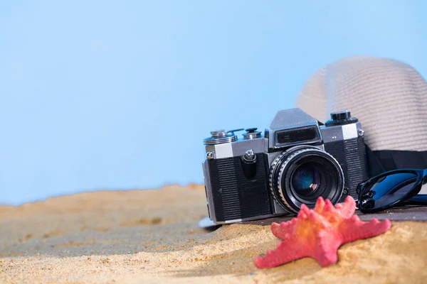 Blue sky. Old photographic film camera. Sunglasses. Sandy sea beach. Summer hat.