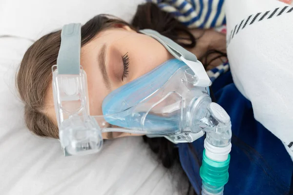 Oxygen mask attached to the respiratory tract. The teenager lies in a hospital bed. A seriously ill young girl.