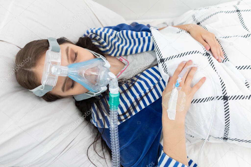 Oxygen mask attached to the respiratory tract. The teenager lies in a hospital bed. A seriously ill young girl.