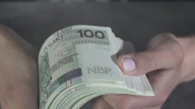 Genç ellerin elinde bir tomar banknot tutarken ve masanın üstünde yelpaze açarken çok yakından görülüyor. Ticari bir alışveriş sırasında masanın üstünde yeni banknotlar açan kadınların yakın görüntüsü..